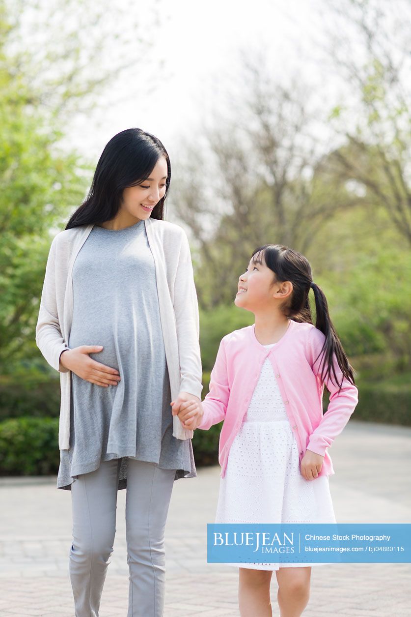 Pregnant Chinese mother and daughter holding hands walking