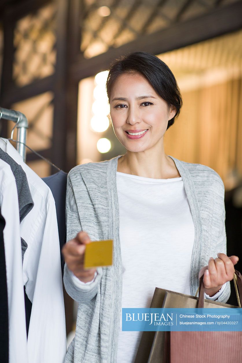 Mature Chinese woman with credit card in clothing store