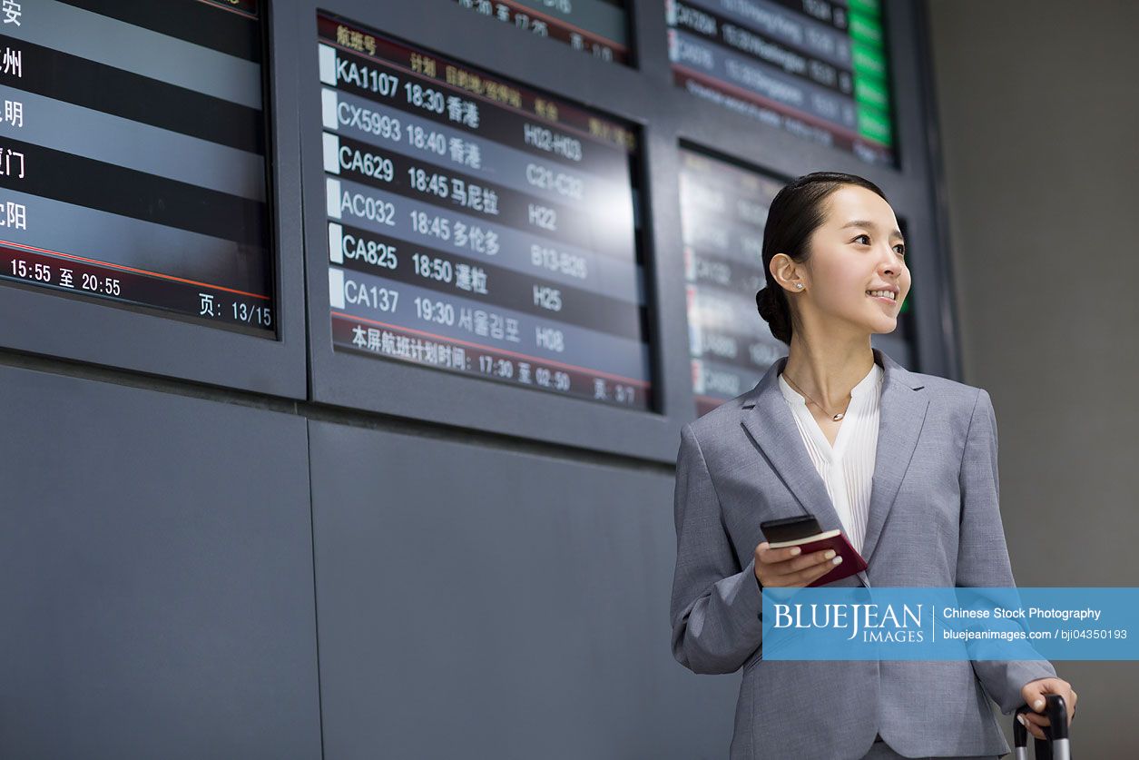 Young Chinese businesswoman holding passport and smart phone in airport