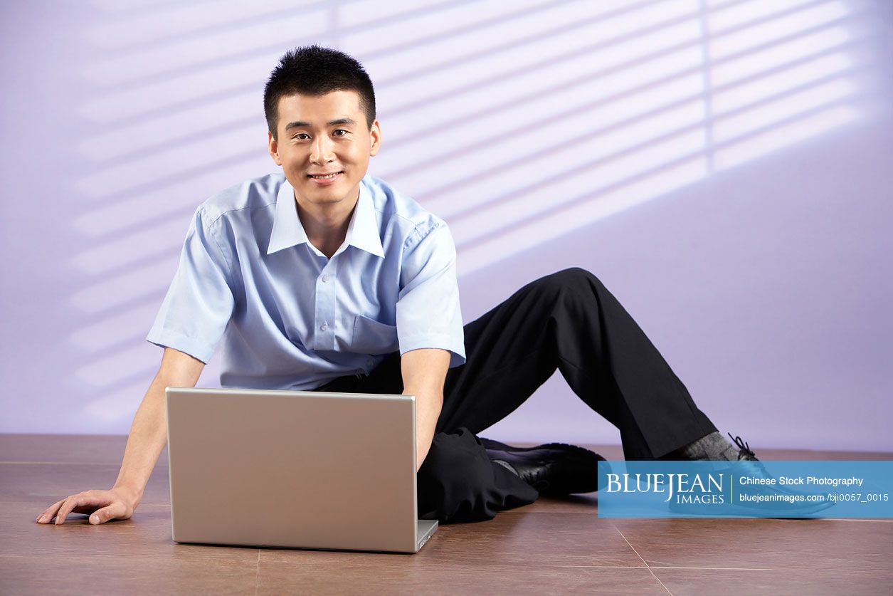 Chinese Man Sitting On Floor With A Computer