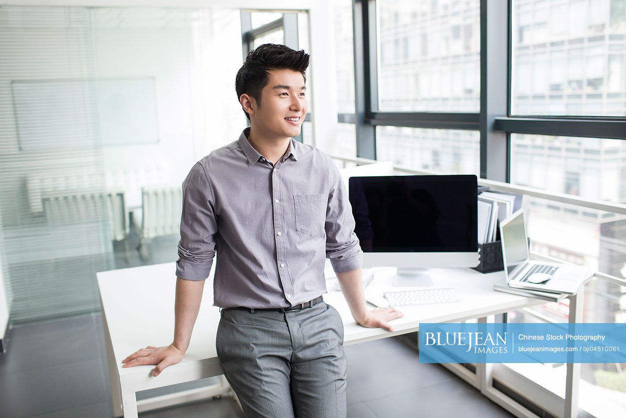 Young Chinese businessman looking through window in office