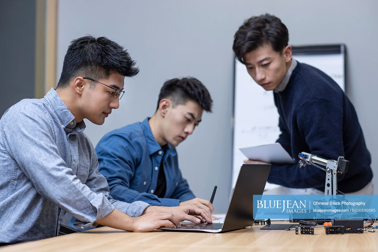 Confident Chinese designers checking a robotic arm