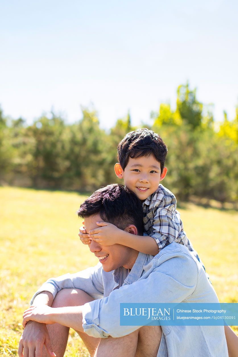 Happy Chinese father and son relaxing on meadow