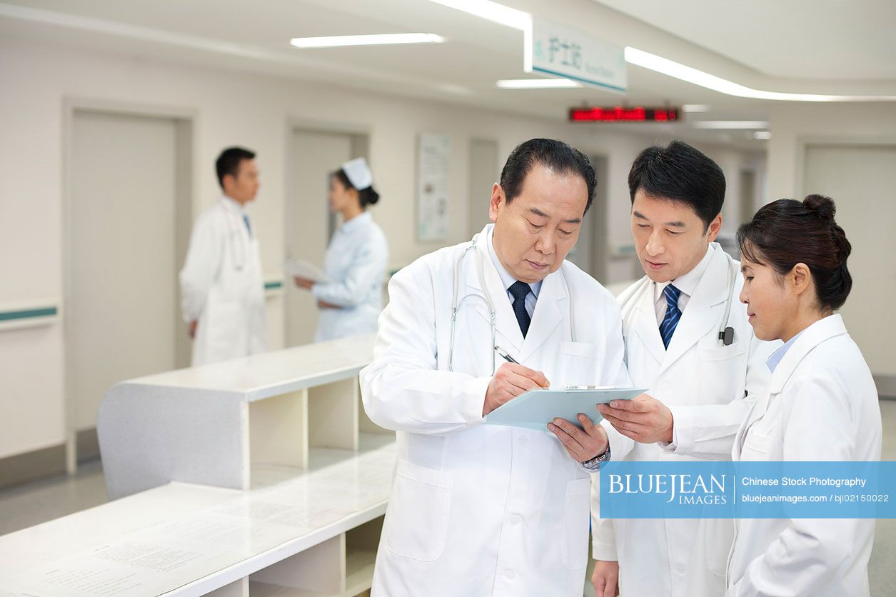 An older Chinese doctor fills out a form with fellow doctors