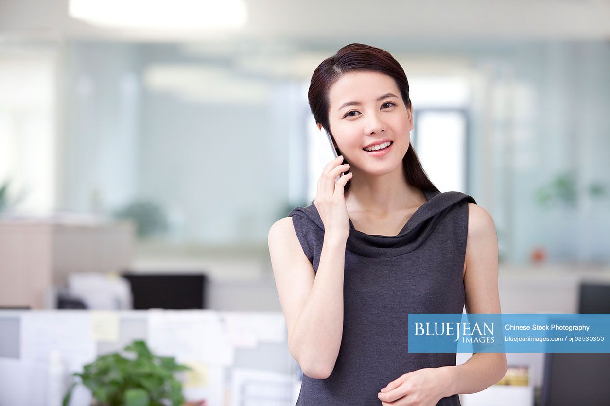 Happy Chinese businesswoman talking on the phone in office