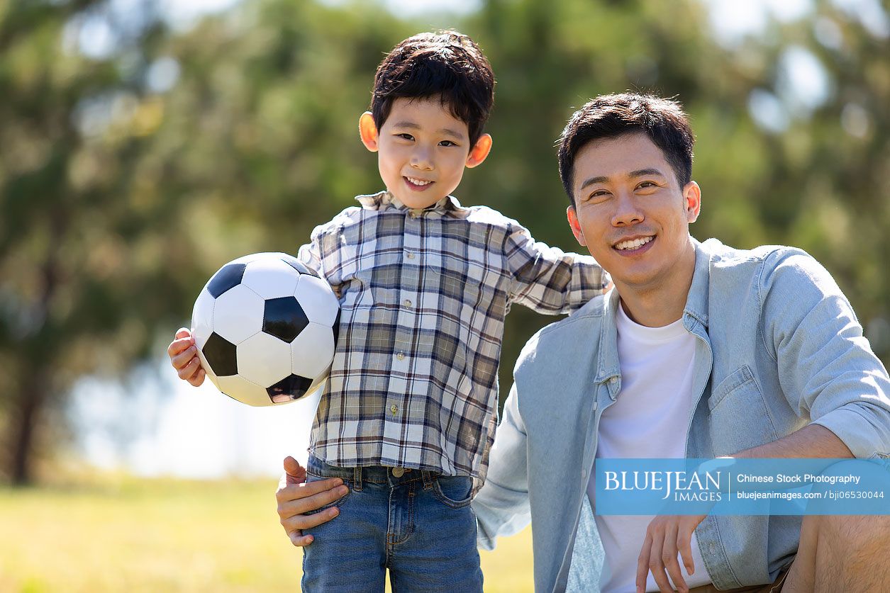 Happy Chinese father and son playing football in park