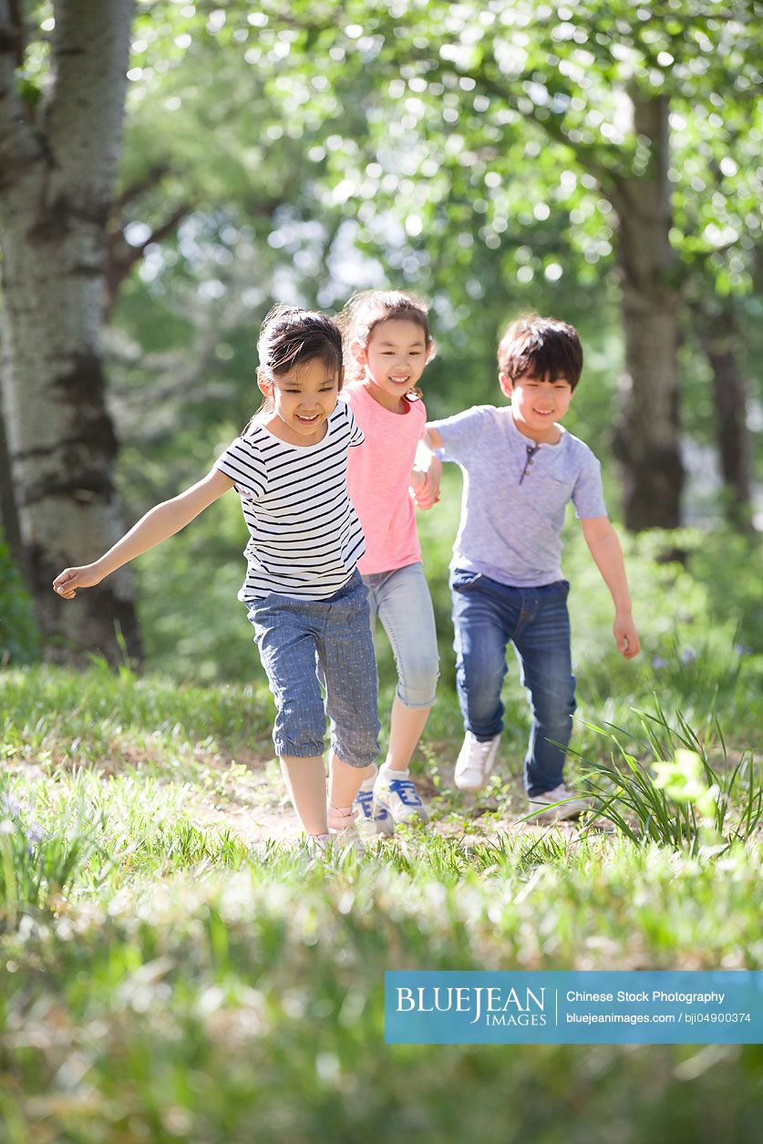 Happy Chinese children holding hands running in woods