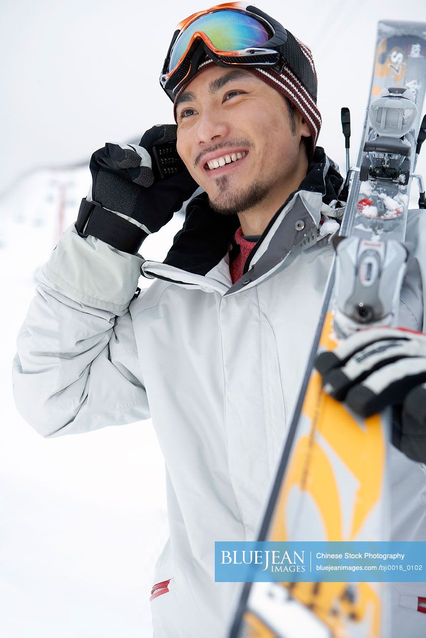 Chinese man holding skis, talking on cell phone
