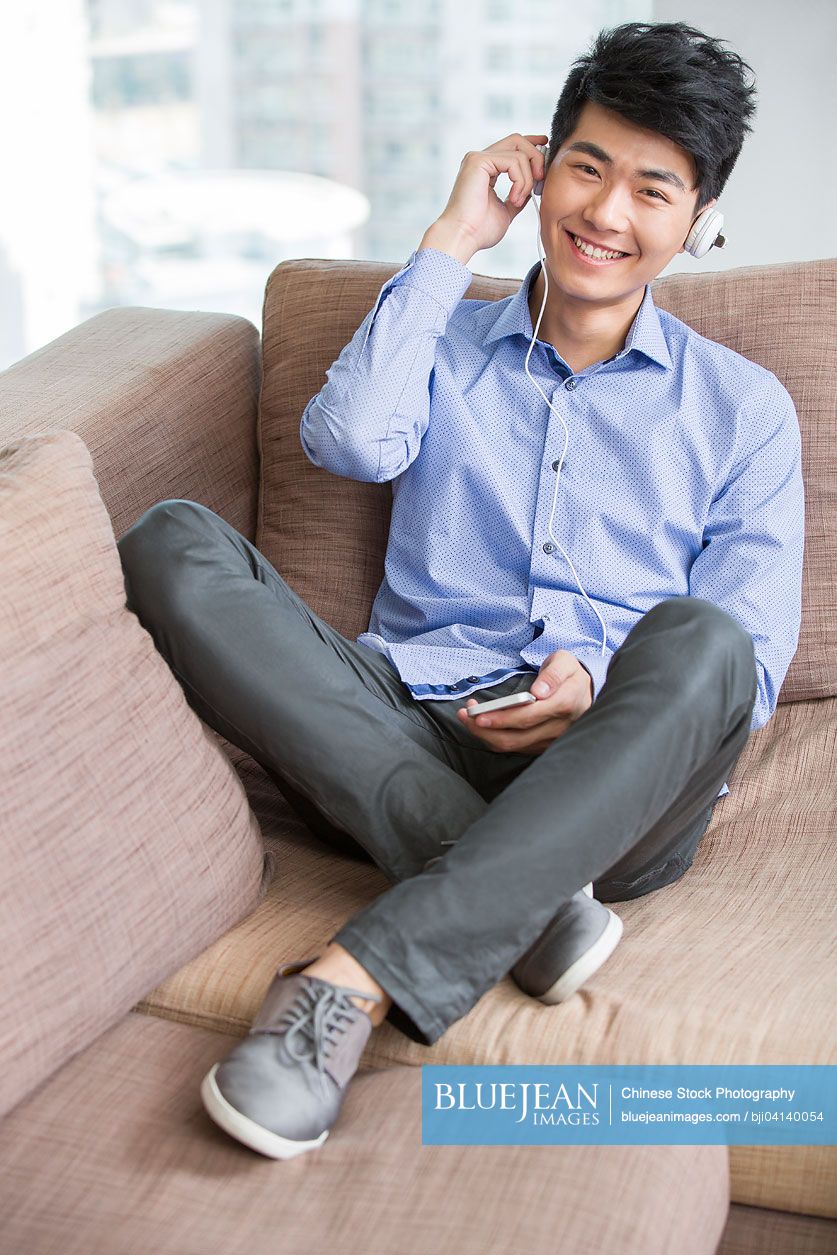 Happy young Chinese man listening to music with smart phone