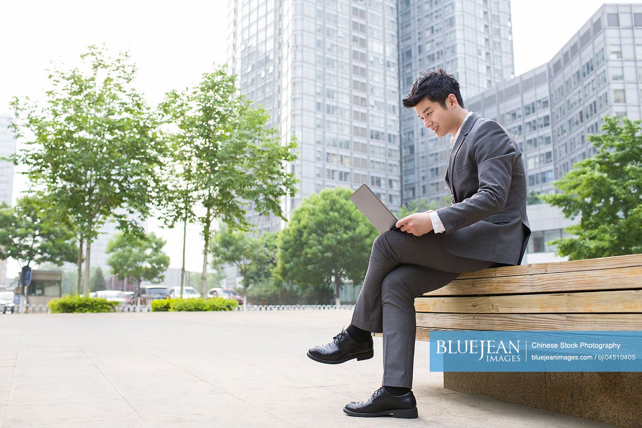 Young Chinese businessman working with laptop outdoors
