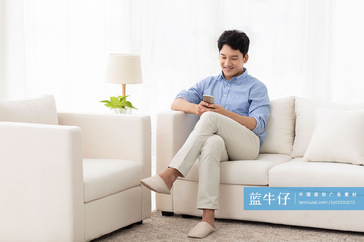 开心的年轻男子坐在沙发上玩手机