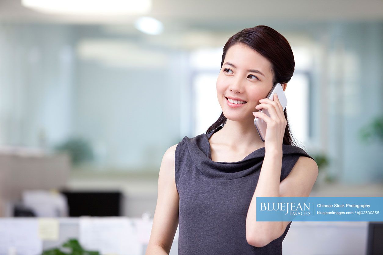 Happy Chinese businesswoman talking on the phone in office