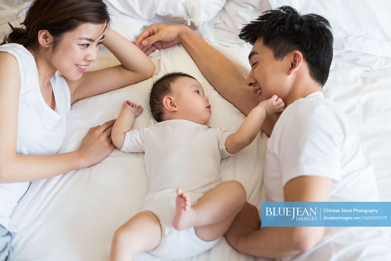 Happy young Chinese family lying on bed