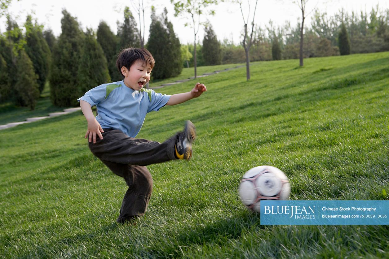 Young Chinese Boy Happily Playing Soccer In The Park