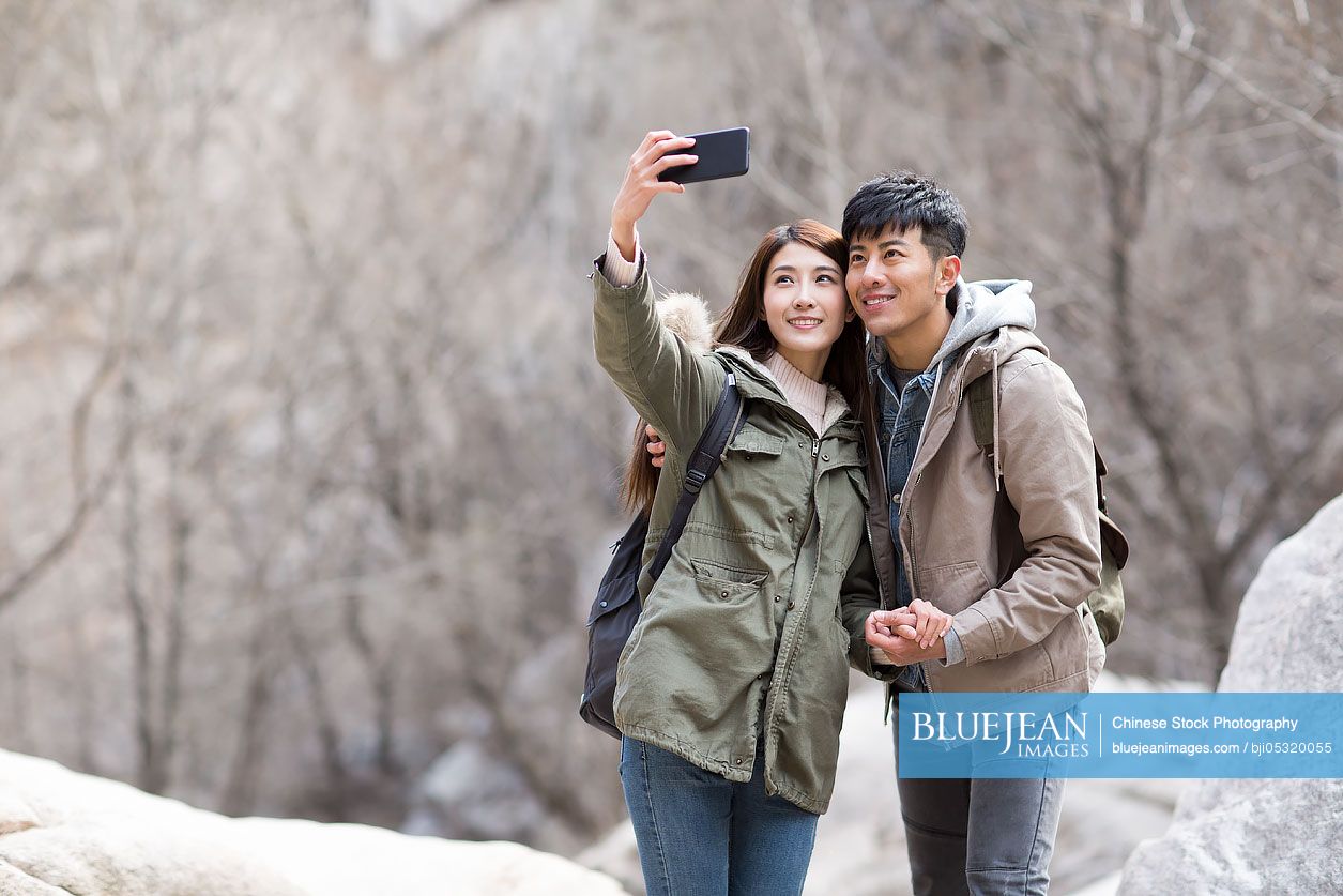 Happy young Chinese couple taking selfies outdoors in winter