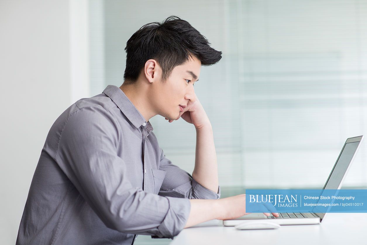 Young Chinese businessman using laptop in office