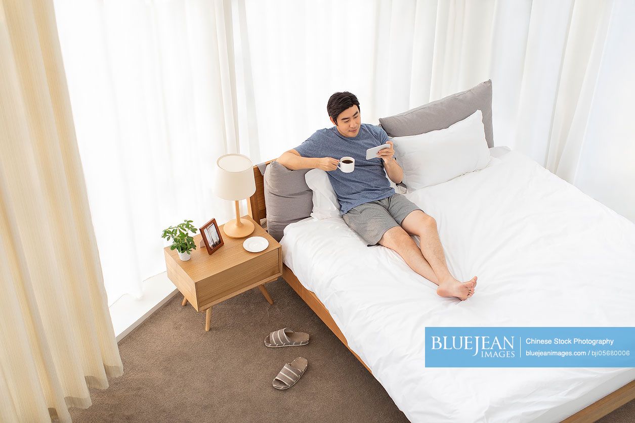 Happy young Chinese man relaxing on bed