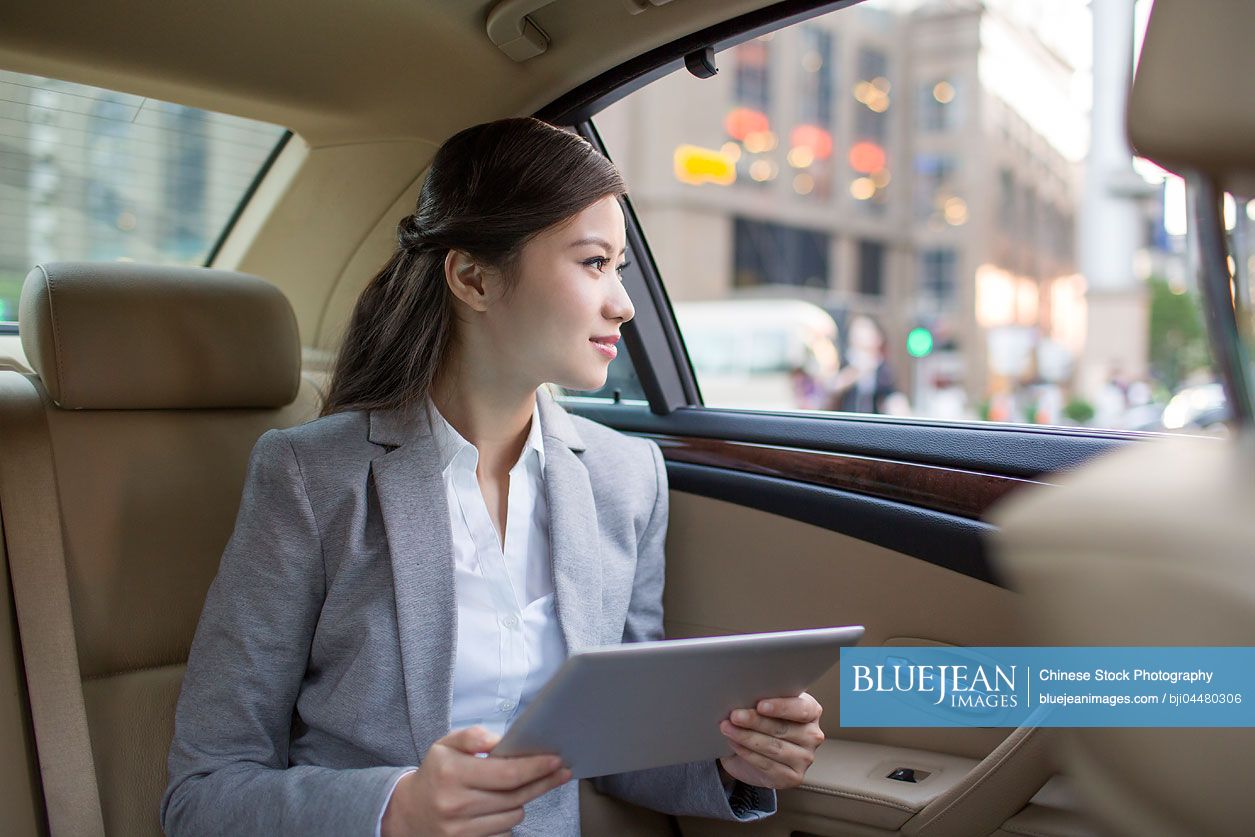 Chinese businesswoman using digital tablet in car back seat