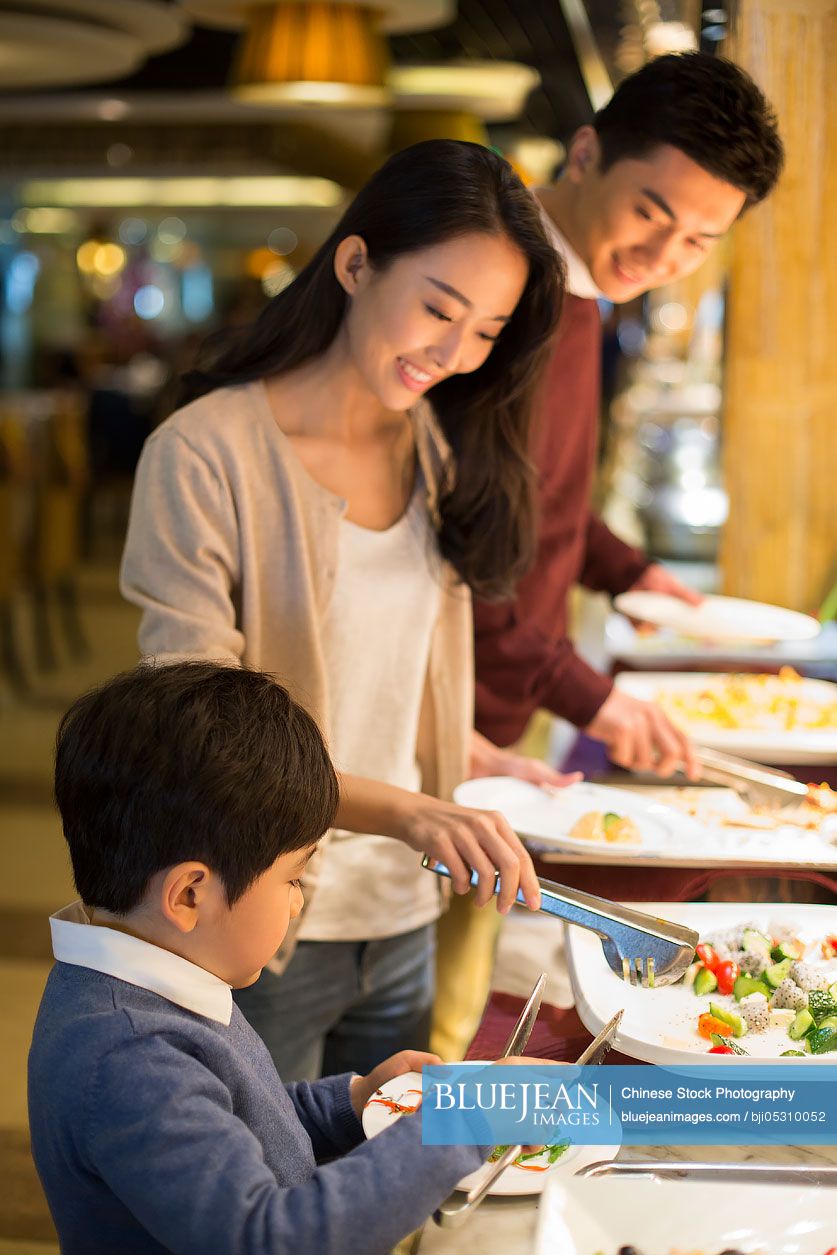 Cheerful young Chinese family taking food from buffet table