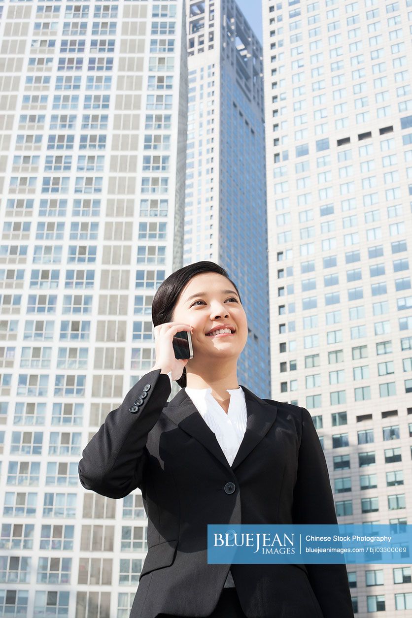 Happy young Chinese businesswoman on the phone in front of tall building