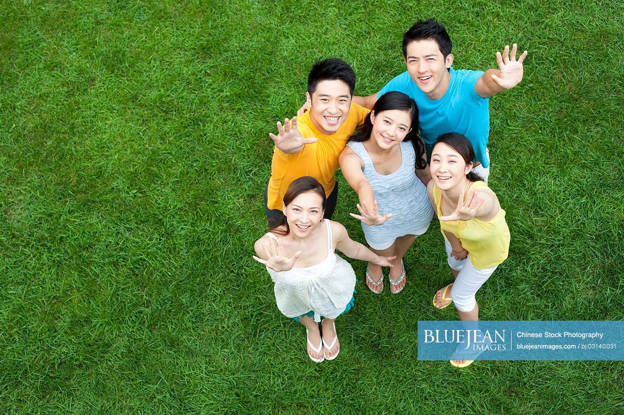 Happy young Chinese standing together on meadow with hands up