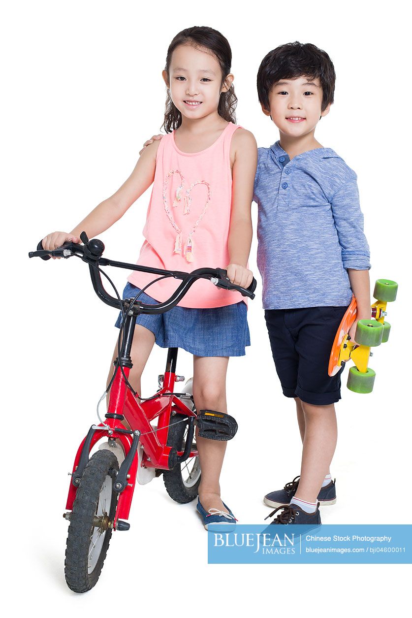 Little Chinese girl riding bike and boy holding a skateboard