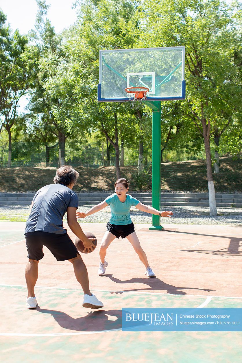 Happy mature Chinese couple playing basketball outdoors