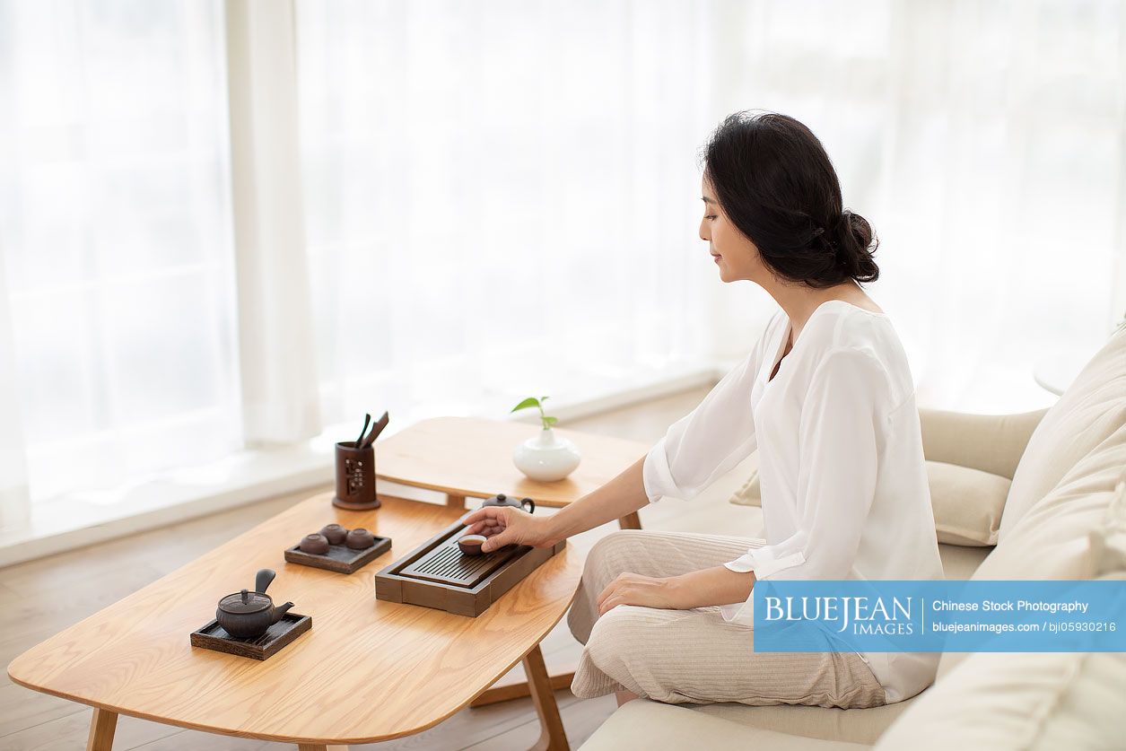 Mature Chinese woman drinking tea in living room