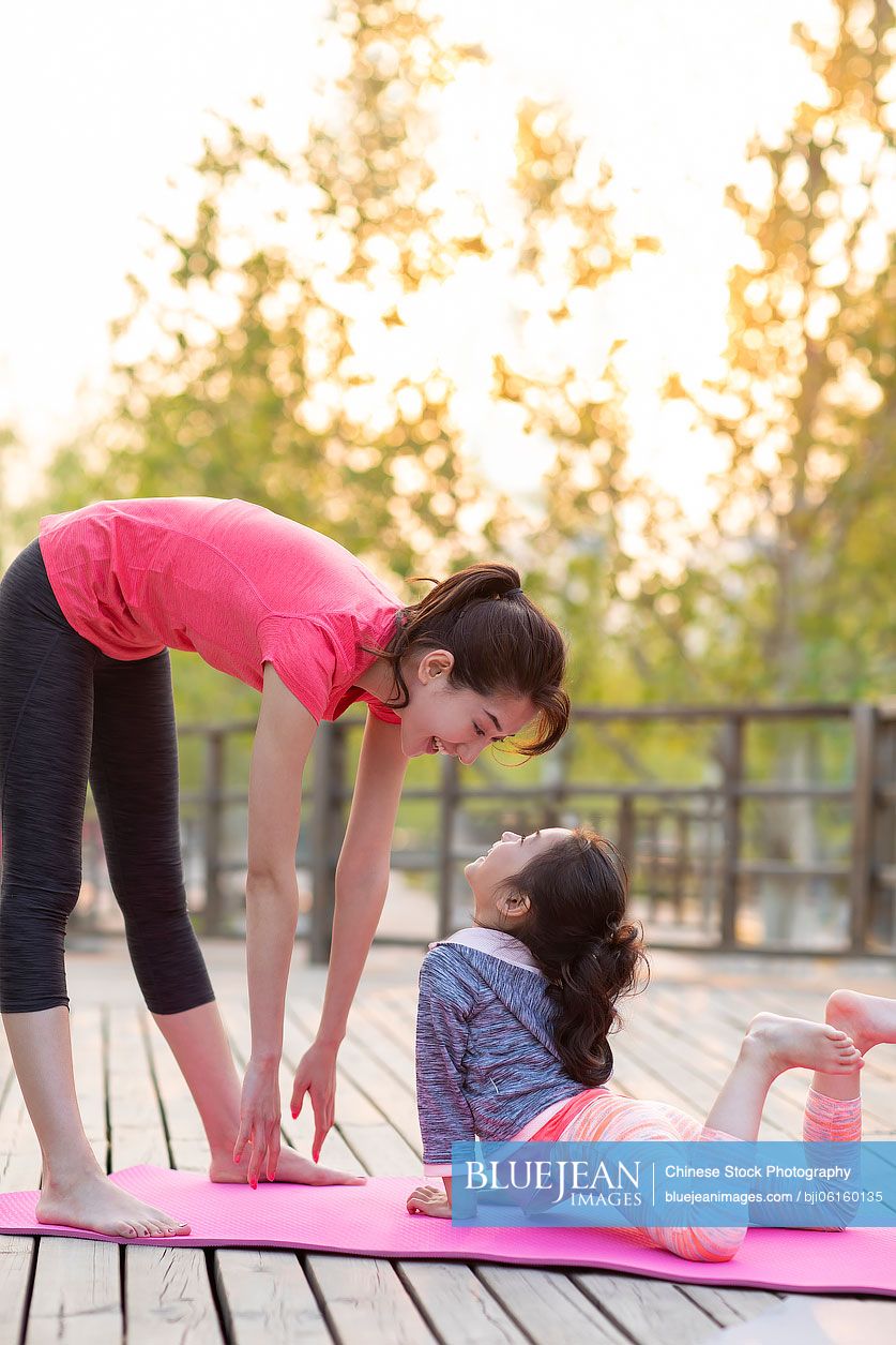Happy Chinese mother and daughter doing yoga outdoors