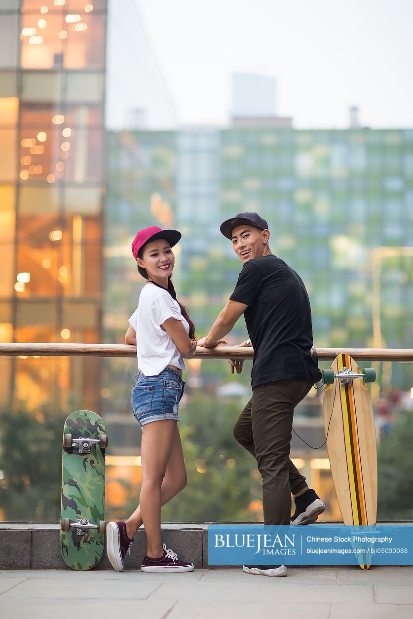 Cheerful young Chinese couple with skateboard dating