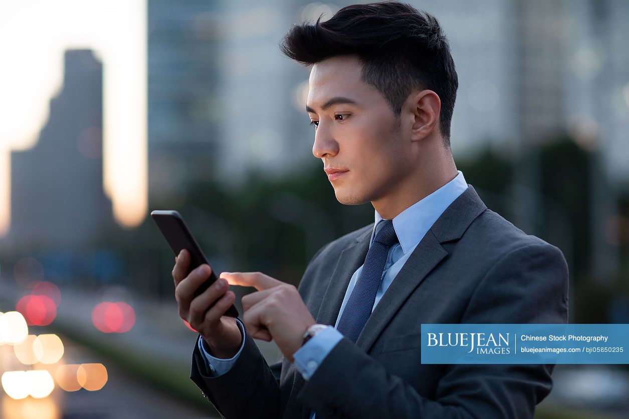 Confident young Chinese businessman using smart phone