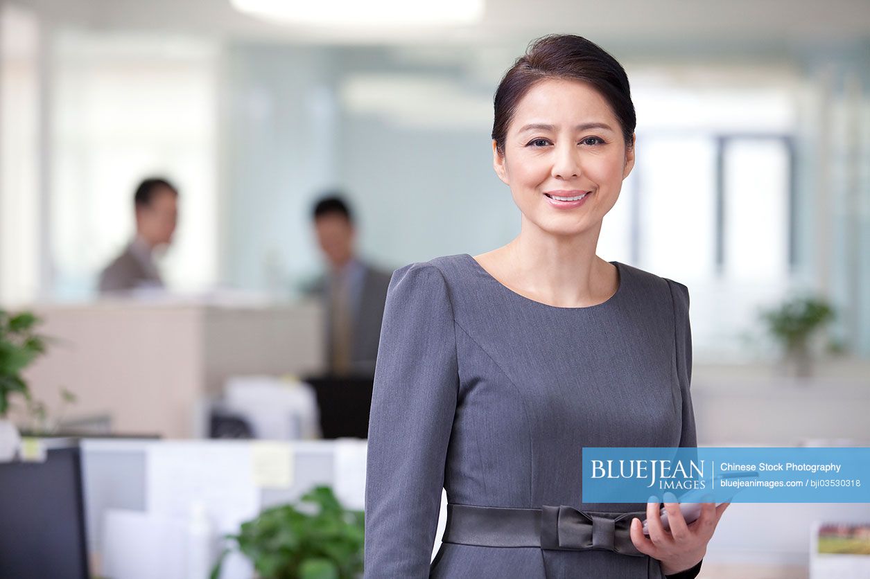 Mature Chinese businesswoman with smart phone in office