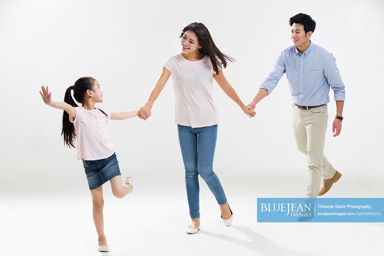 Cheerful young Chinese family holding hands running