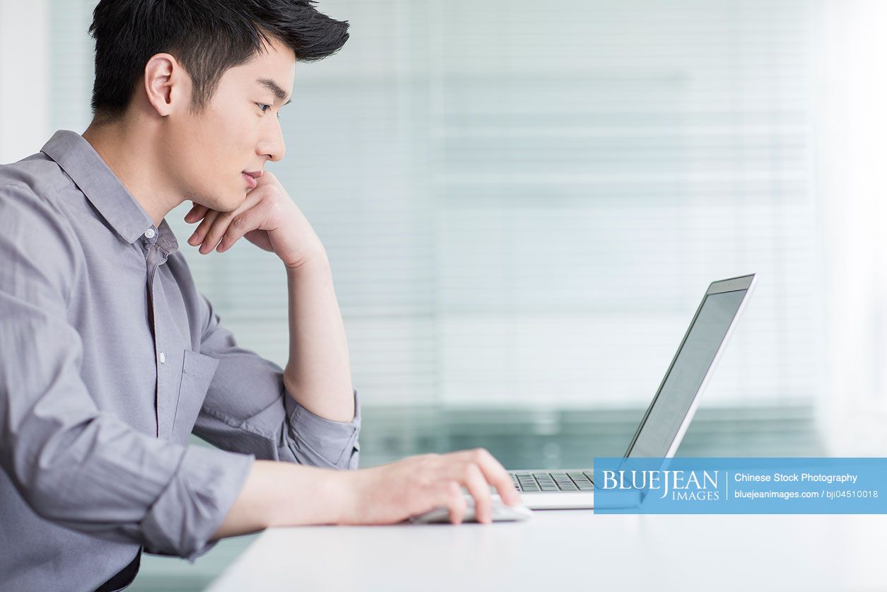 Young Chinese businessman using laptop in office