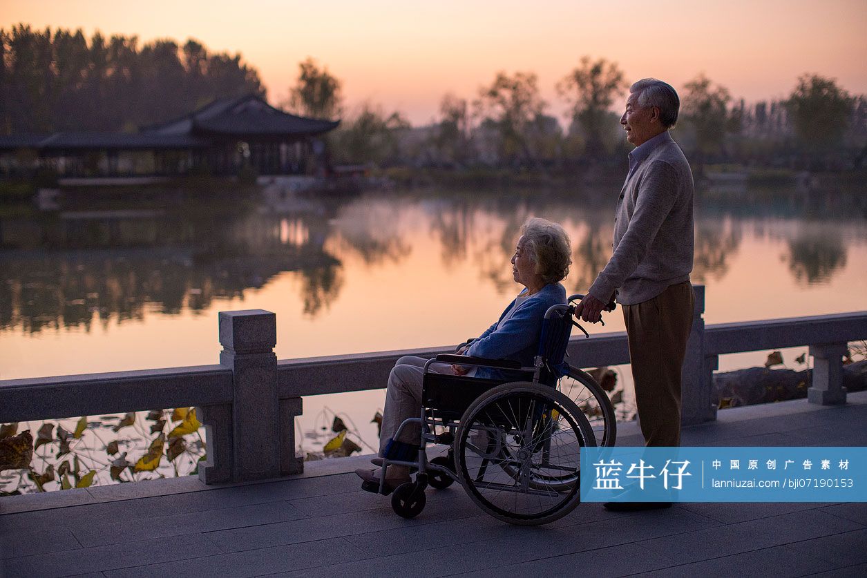 老年男子推着坐轮椅的妻子逛公园