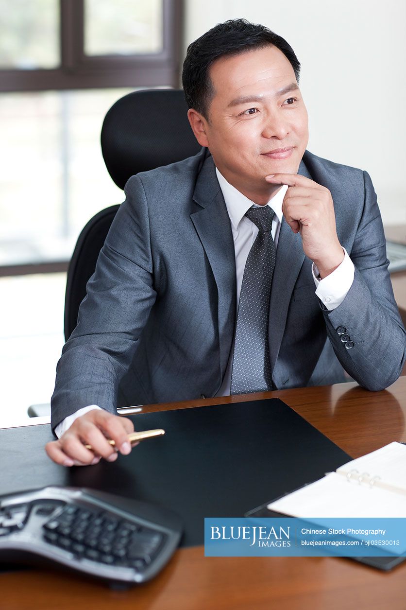 Mature Chinese businessman in office, hand on chin