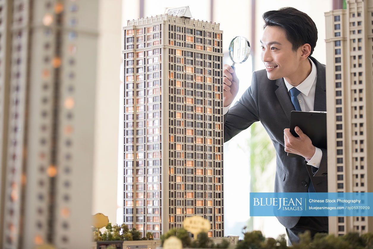 Chinese realtor checking architectural model through magnifying glass