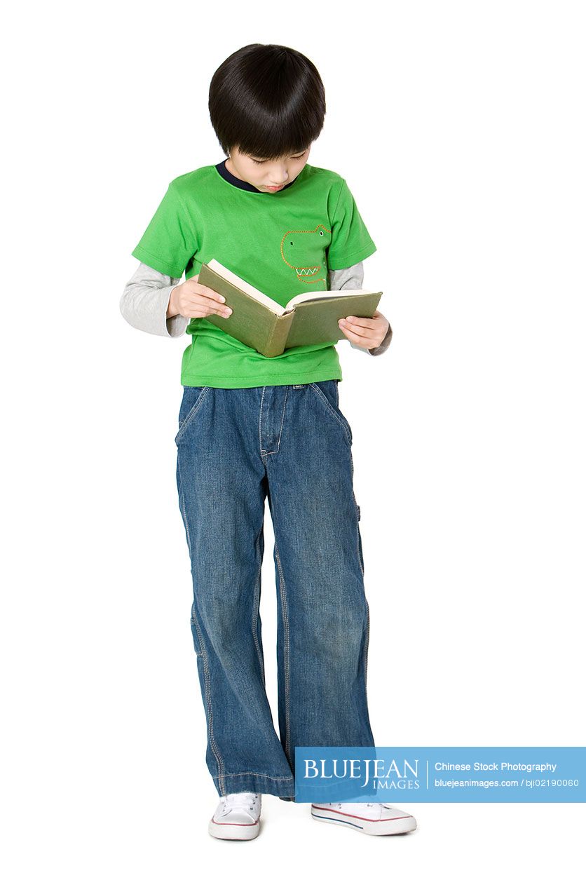 Young Chinese boy standing and reading a book
