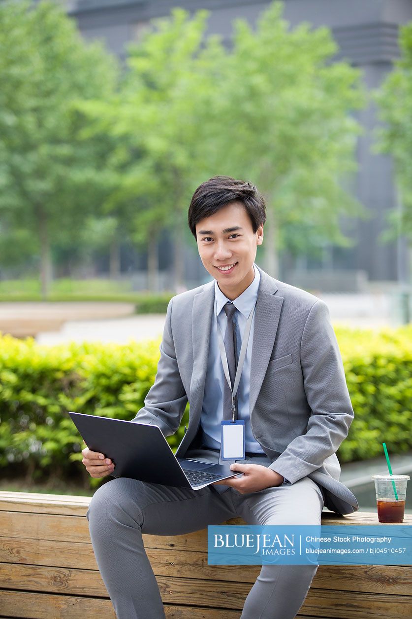 Young Chinese businessman working with laptop outdoors