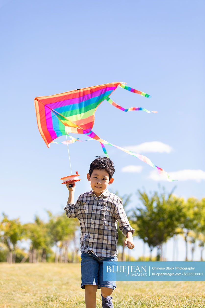 Happy Chinese boy running with kite on meadow