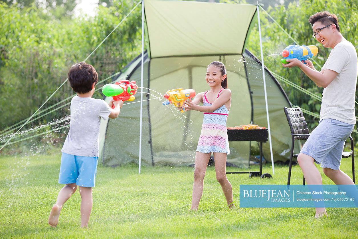 Happy Chinese father and children playing squirt guns