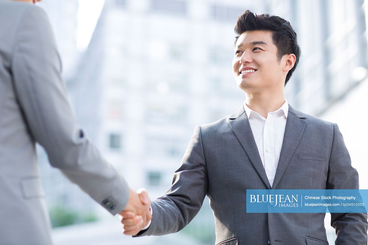 Young Chinese business person shaking hands outdoors