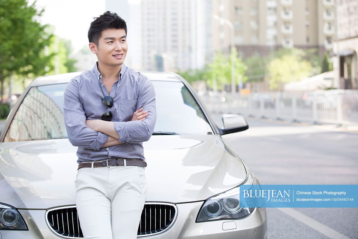 Young Chinese man leaning against his car