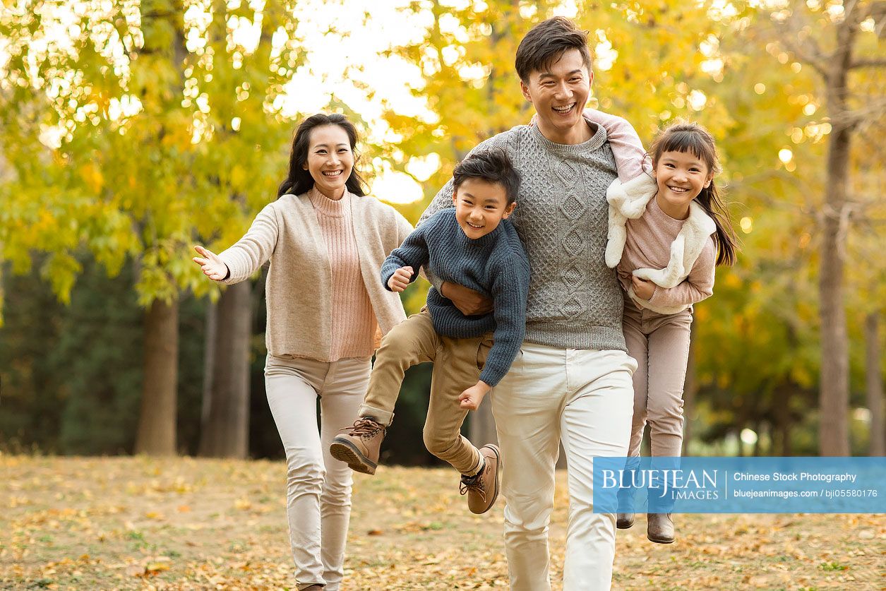 Happy young Chinese family playing in autumn woods