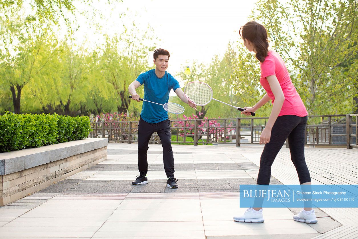 Happy young Chinese couple playing badminton in park