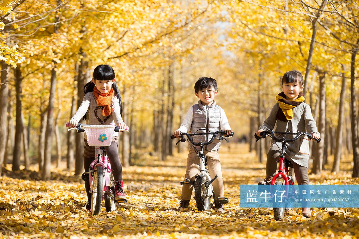 三个小孩在秋日的树林里骑自行车