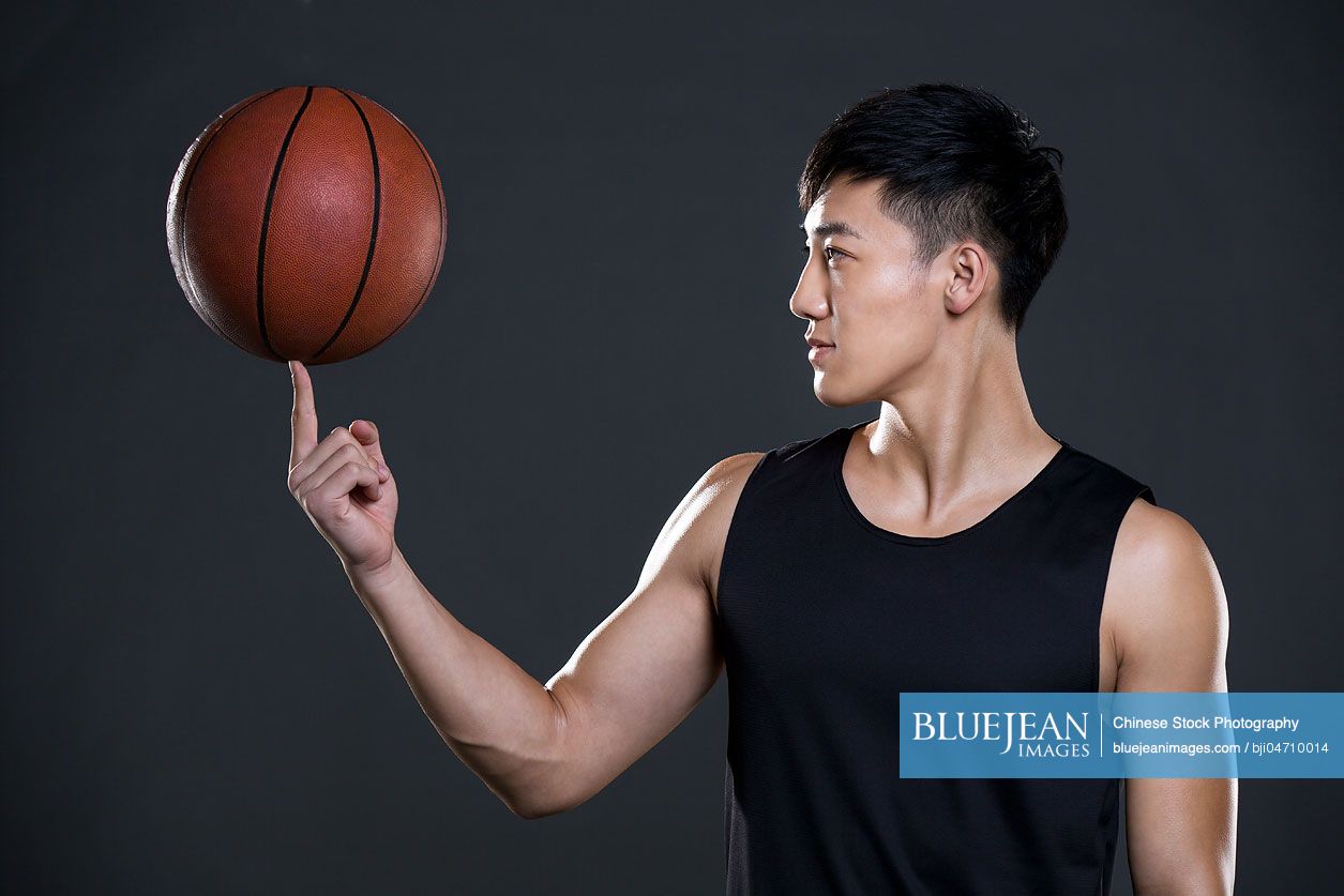 Young Chinese man spinning basketball on finger