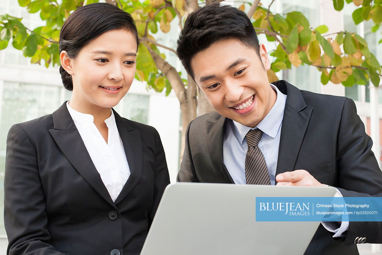 Happy young Chinese business partners using laptop outdoors