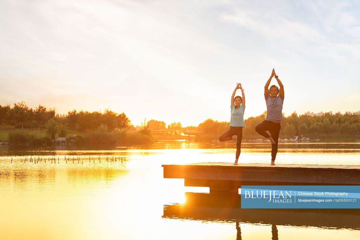 Happy mature Chinese couple doing yoga in park