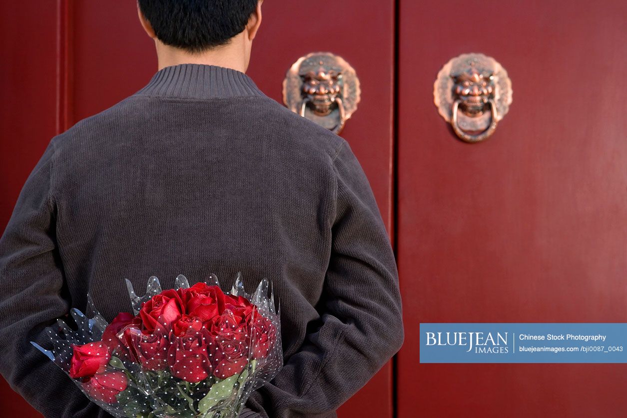 Chinese Young Man Waiting At Front Door With A Bunch Of Roses Behind His Back